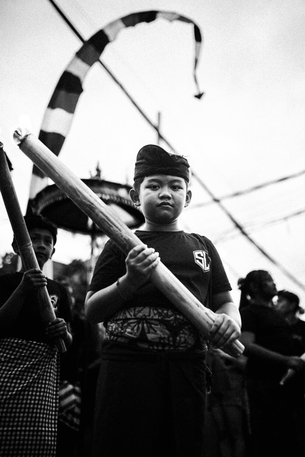 Des enfants portant des vêtements traditionnels, tenant des bâtons, dans une scène en noir et blanc.