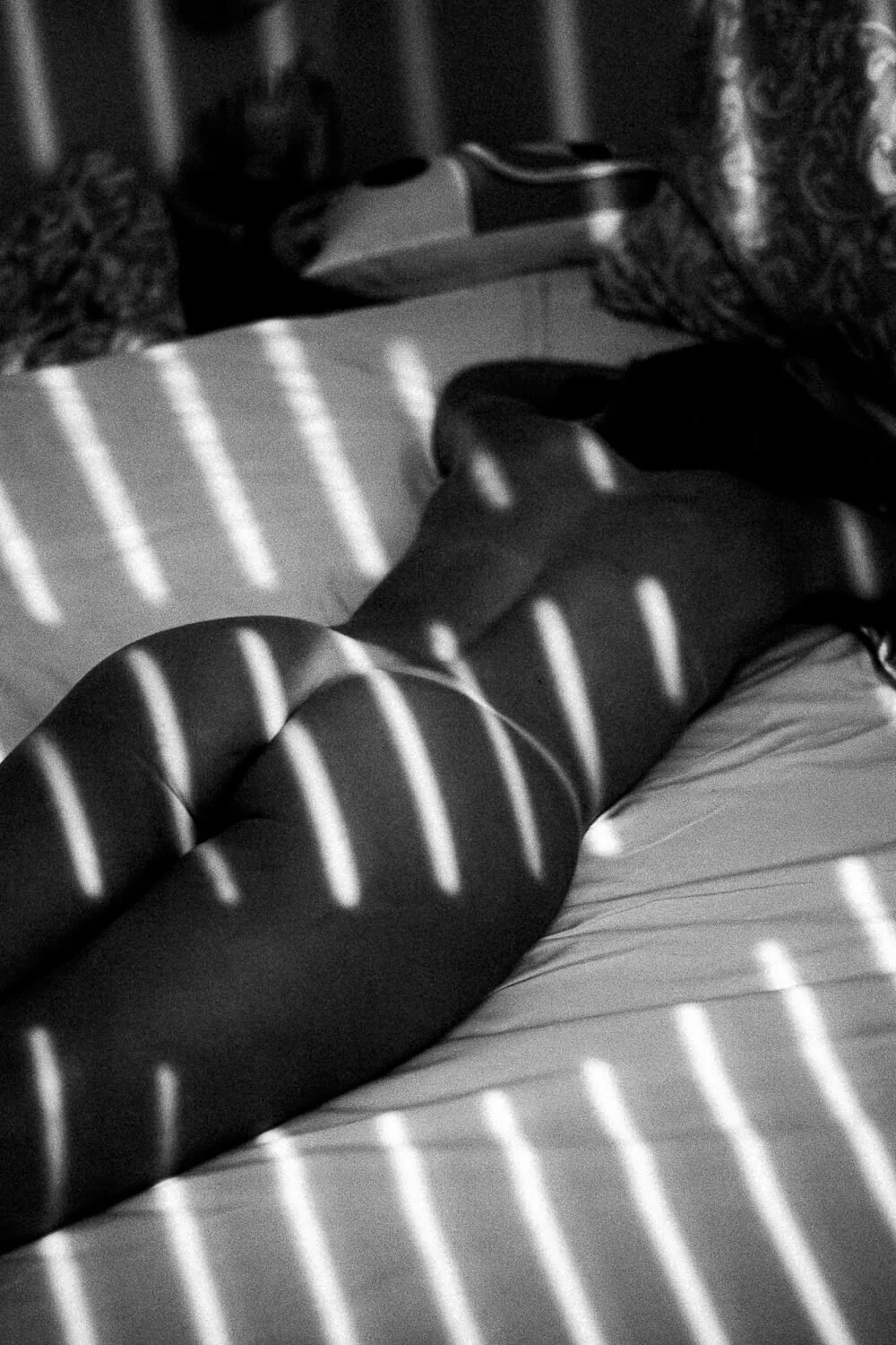 A person lying on a bed with shadows of blinds cast across their body and the bed.