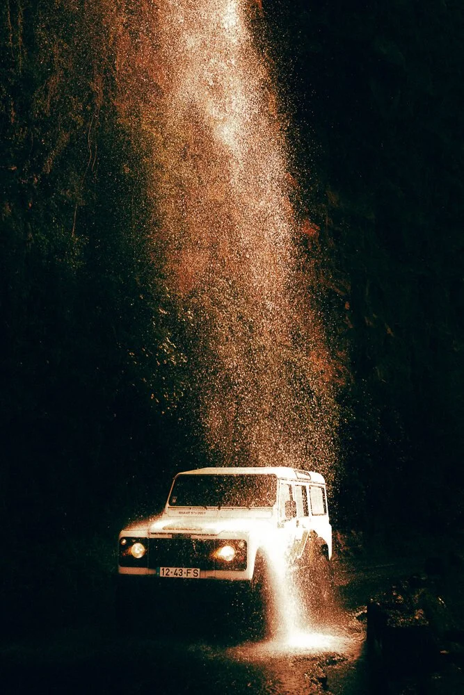 A white off-road vehicle driving through water with water splashing and spray in the air at night.