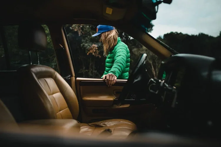 Personne en vêtements verts et casquette bleue regardant dehors à travers la fenêtre d'un véhicule.