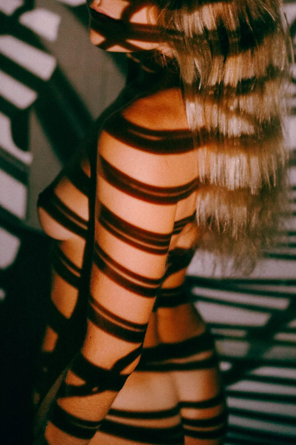 A woman with wavy blonde hair wearing a black dress with cut-out horizontal stripes.