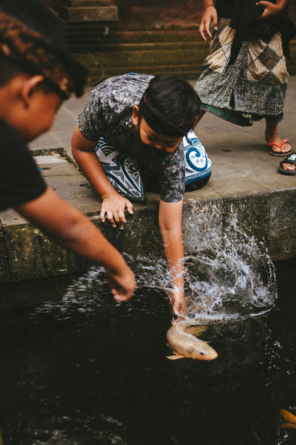 Jeune garçon pêchant un poisson dans une rivière avec d'autres enfants autour.