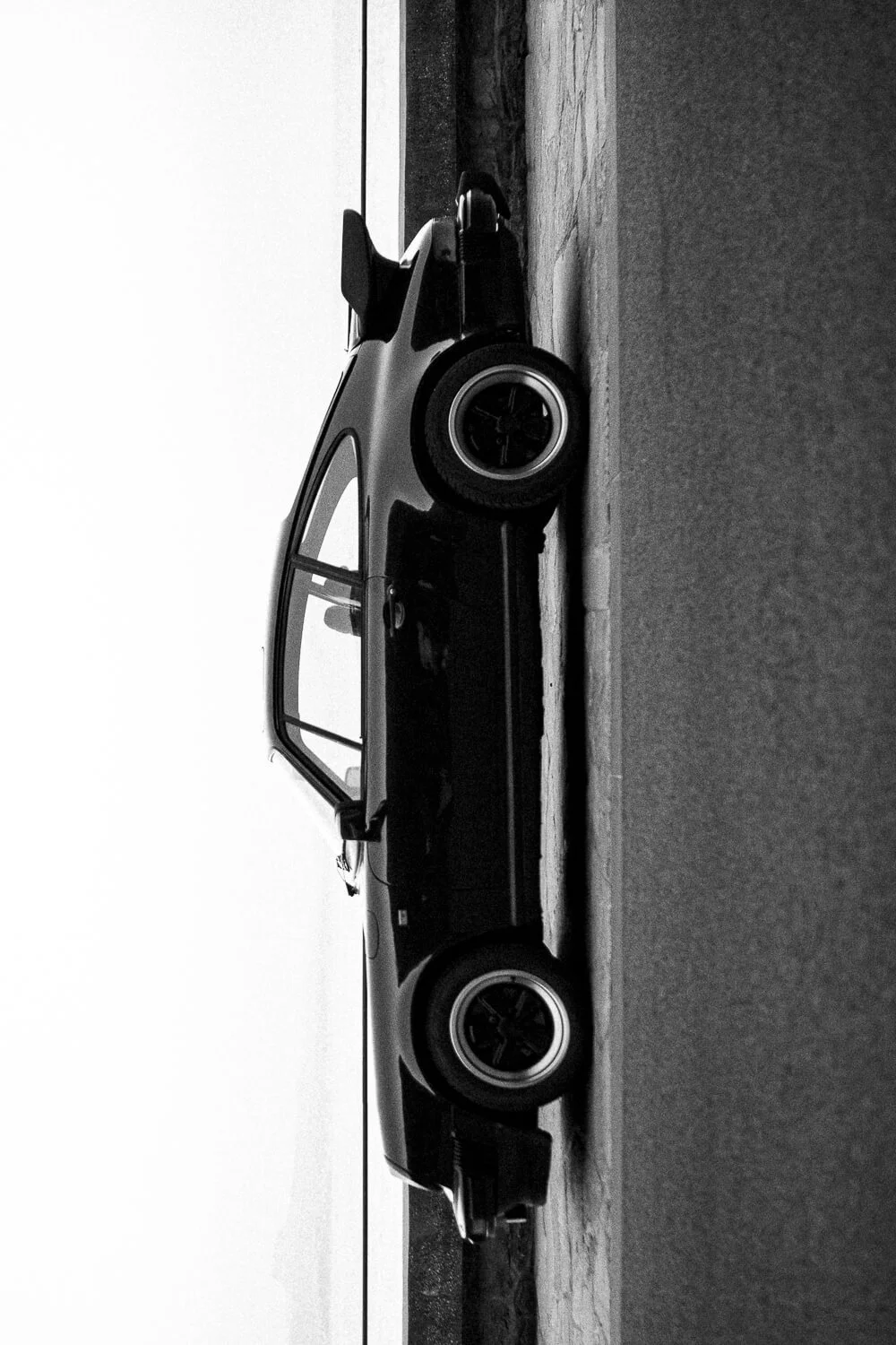 Black and white photo of a vintage sports car parked on a paved surface with a plain sky background.