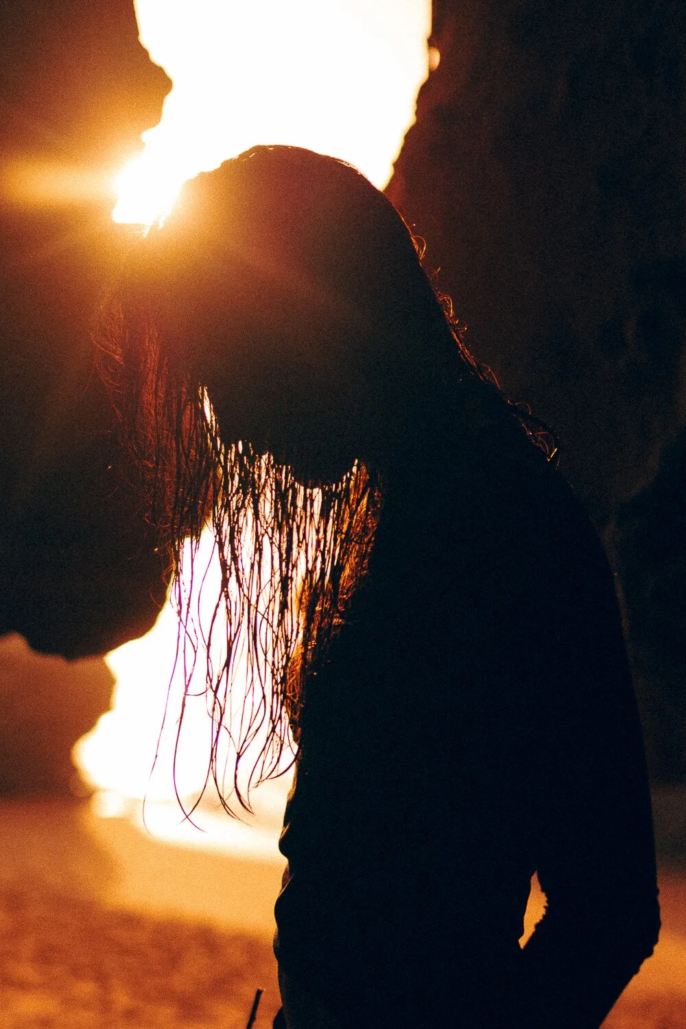 Silhouette of a woman with wet hair on a beach at sunset, backlit by a bright fiery sky.