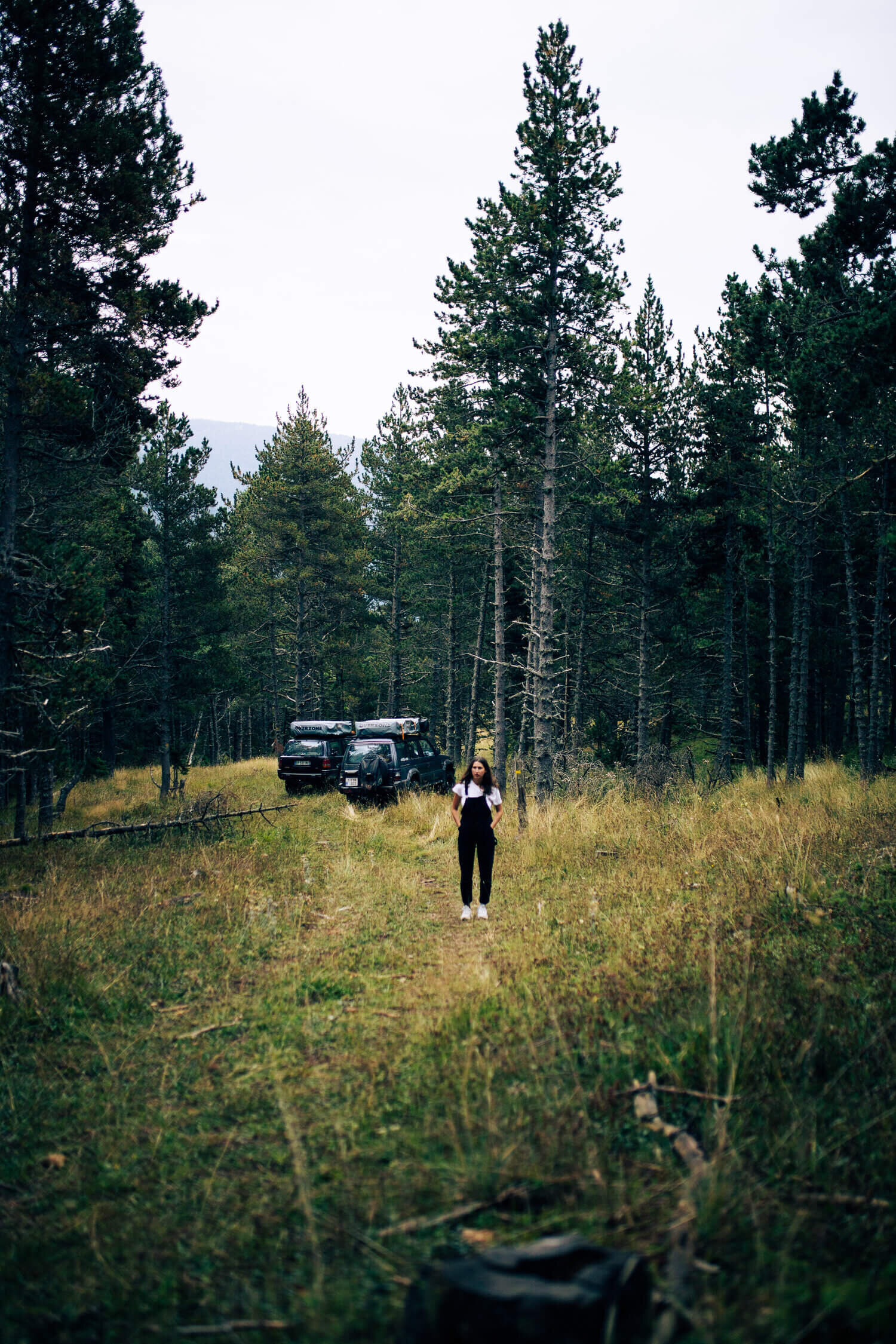 Une femme marchant sur un sentier forestier avec deux véhicules tout-terrain à l'arrière-plan dans une forêt dense.