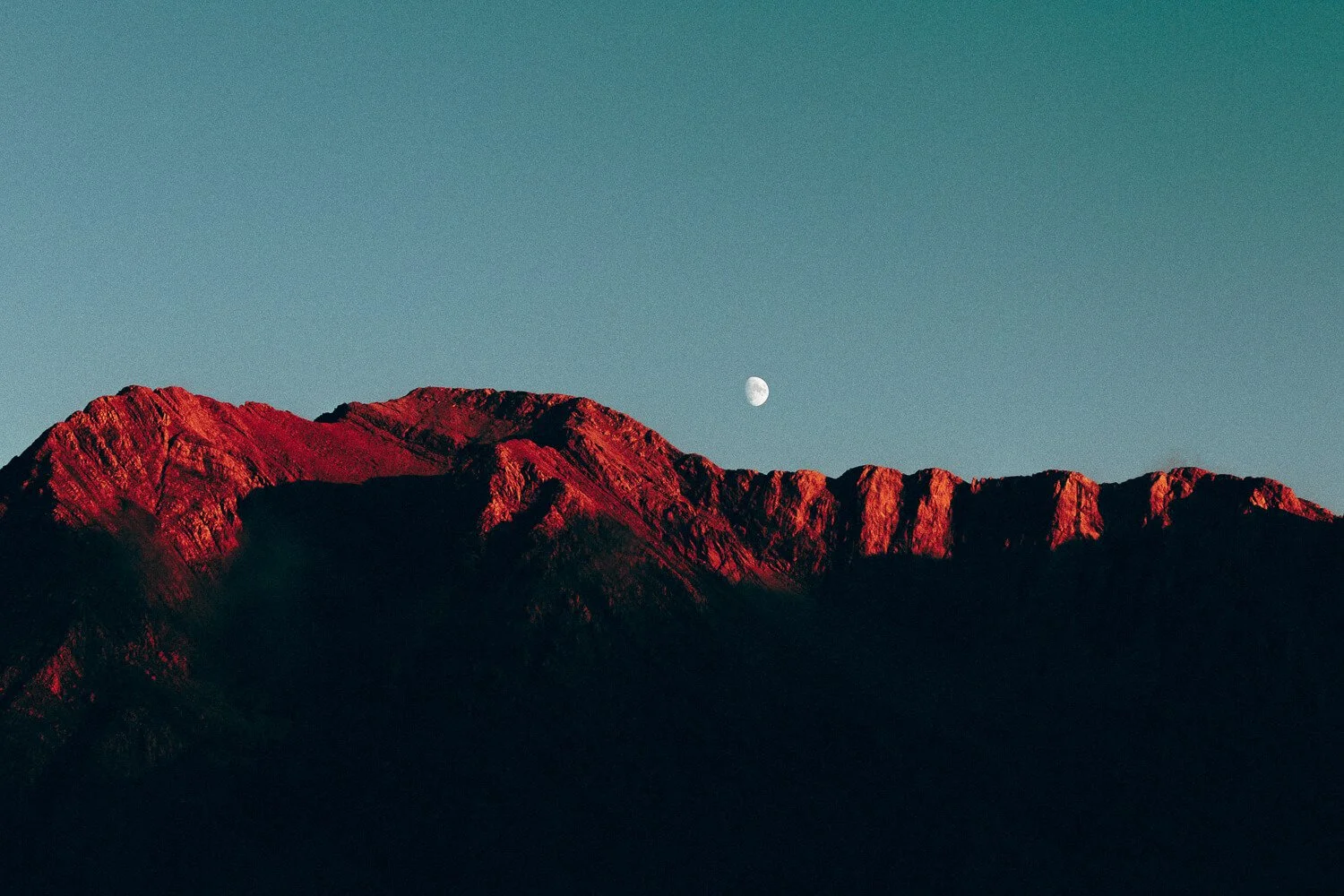 Montagnes rocheuses sous la lumière du coucher de soleil avec la lune visible dans le ciel clair