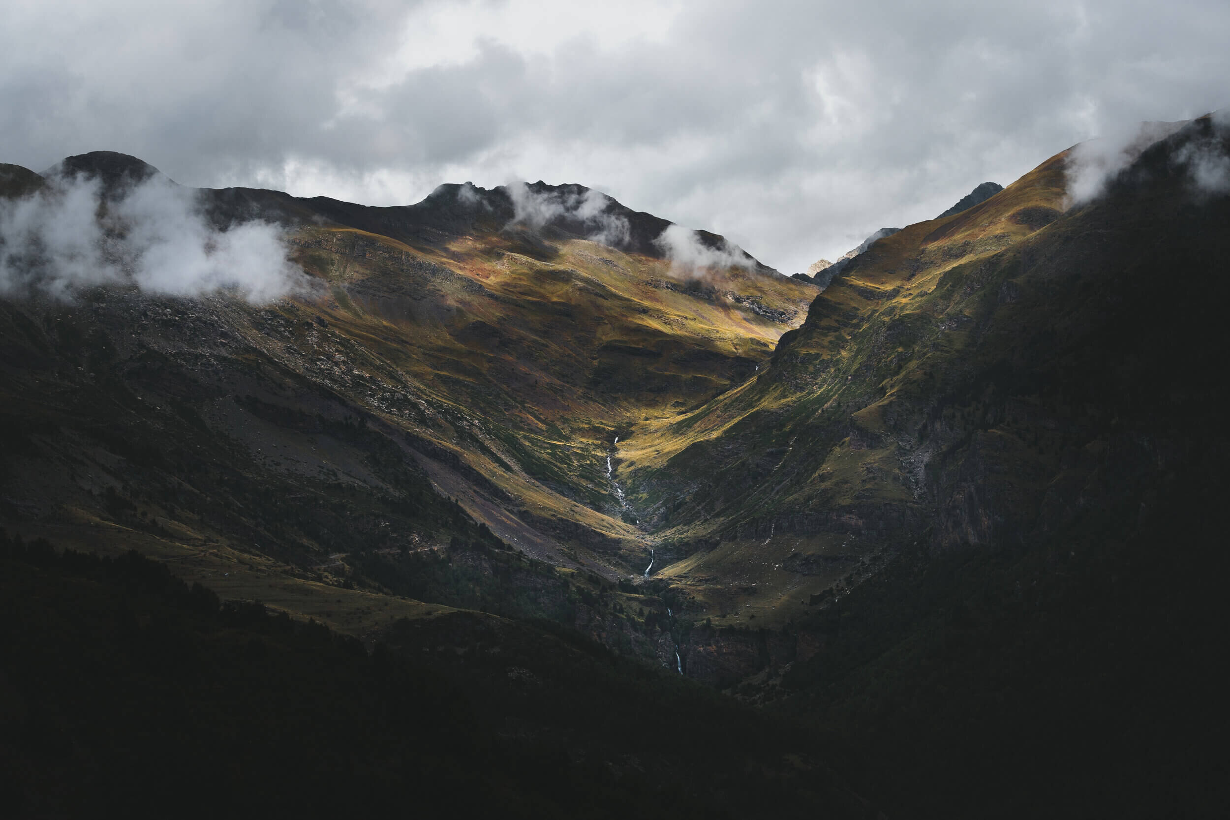 Paysage de montagnes couvertes de végétation avec des nuages et un ciel couvert.