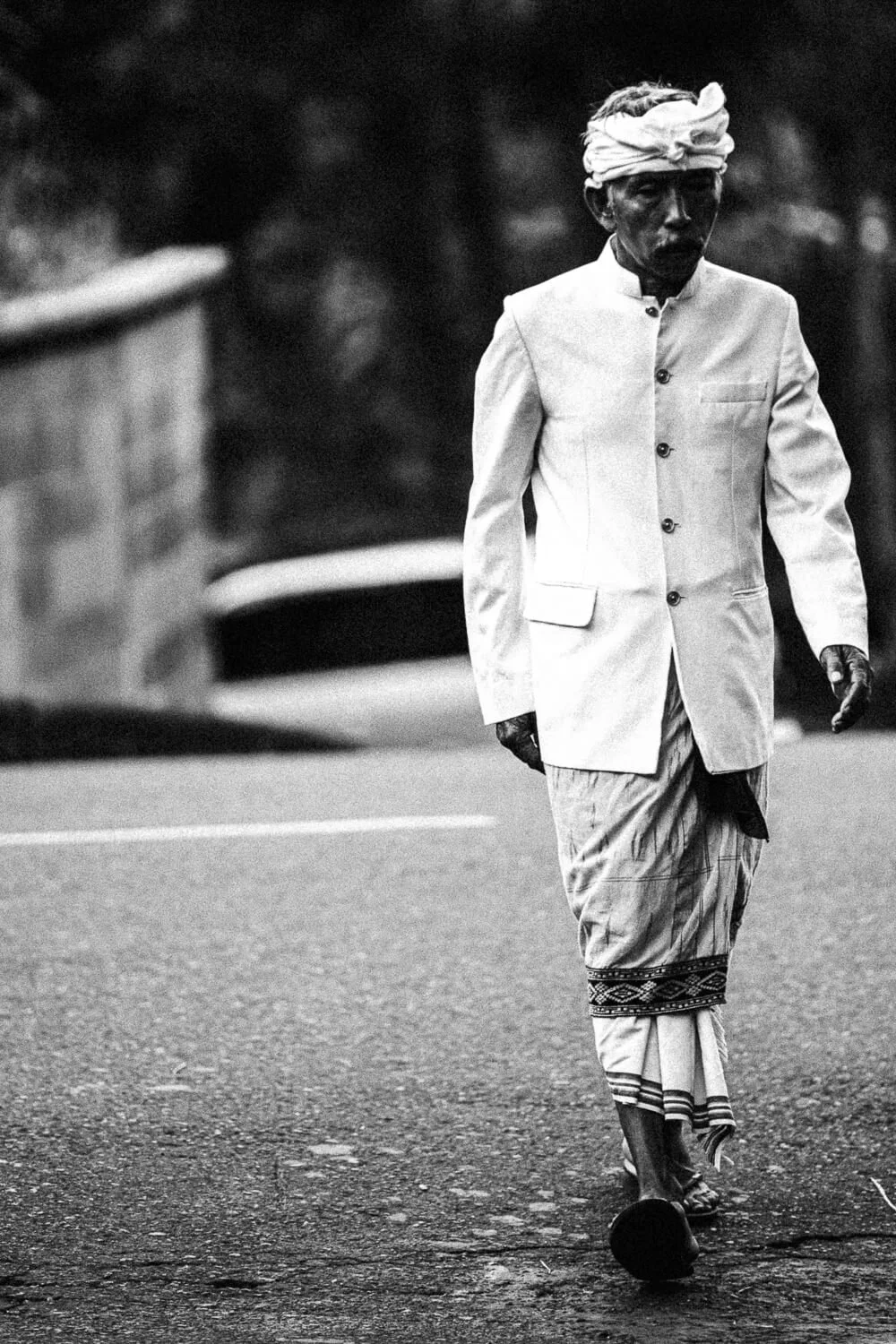 Un homme portant une robe traditionnelle et un turban marche sur une route, image en noir et blanc.