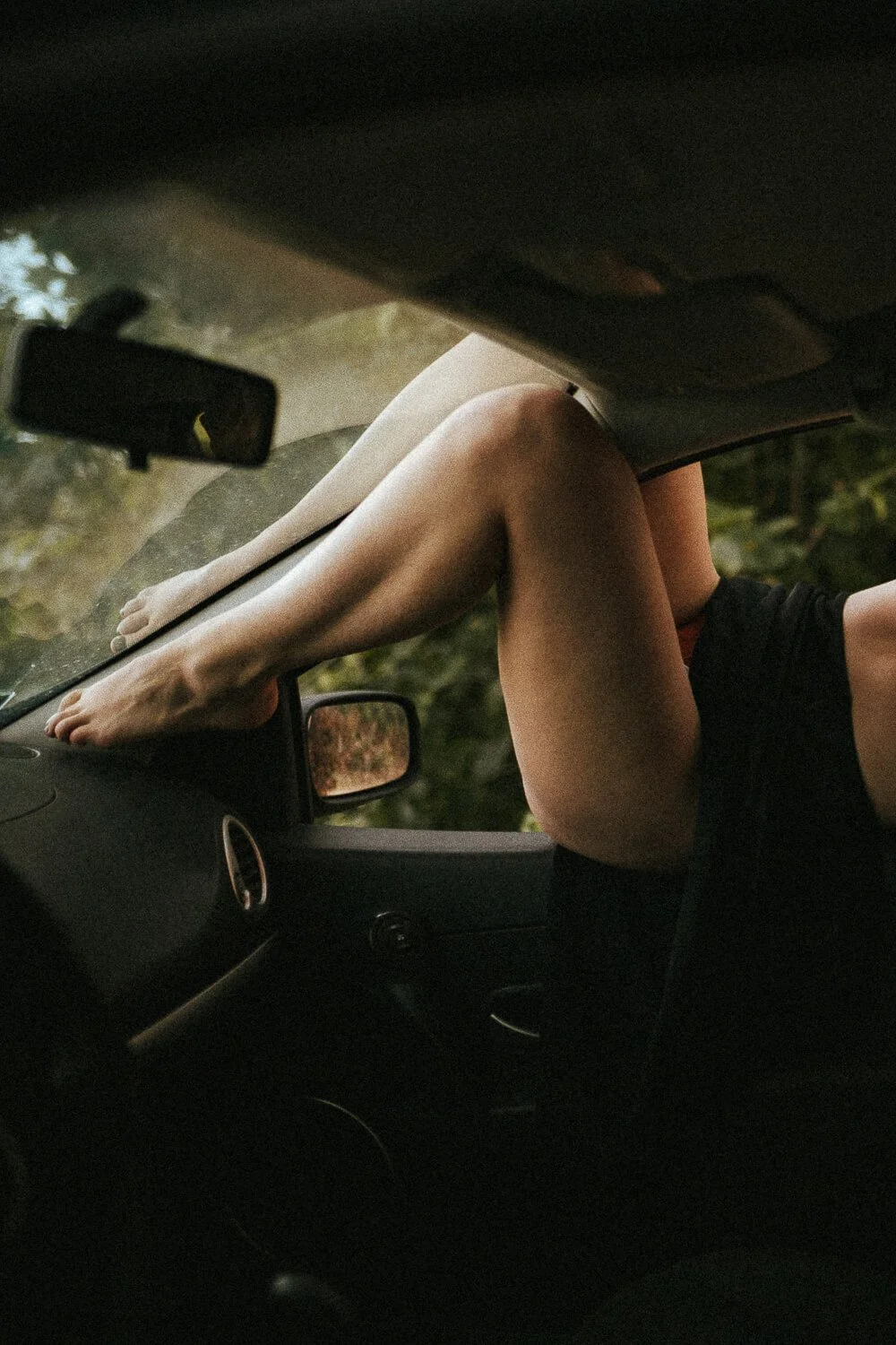 Person with bare legs resting on a car's dashboard with their feet inside the car and sitting back in the driver's seat.