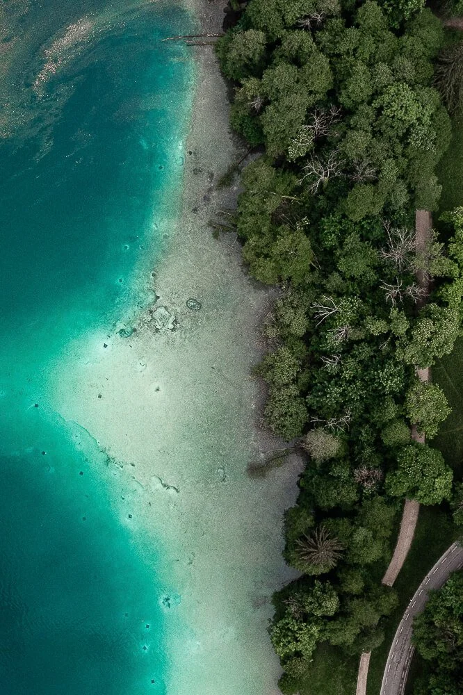 Aerial view of a shoreline with clear turquoise water and dense green trees along the coast.