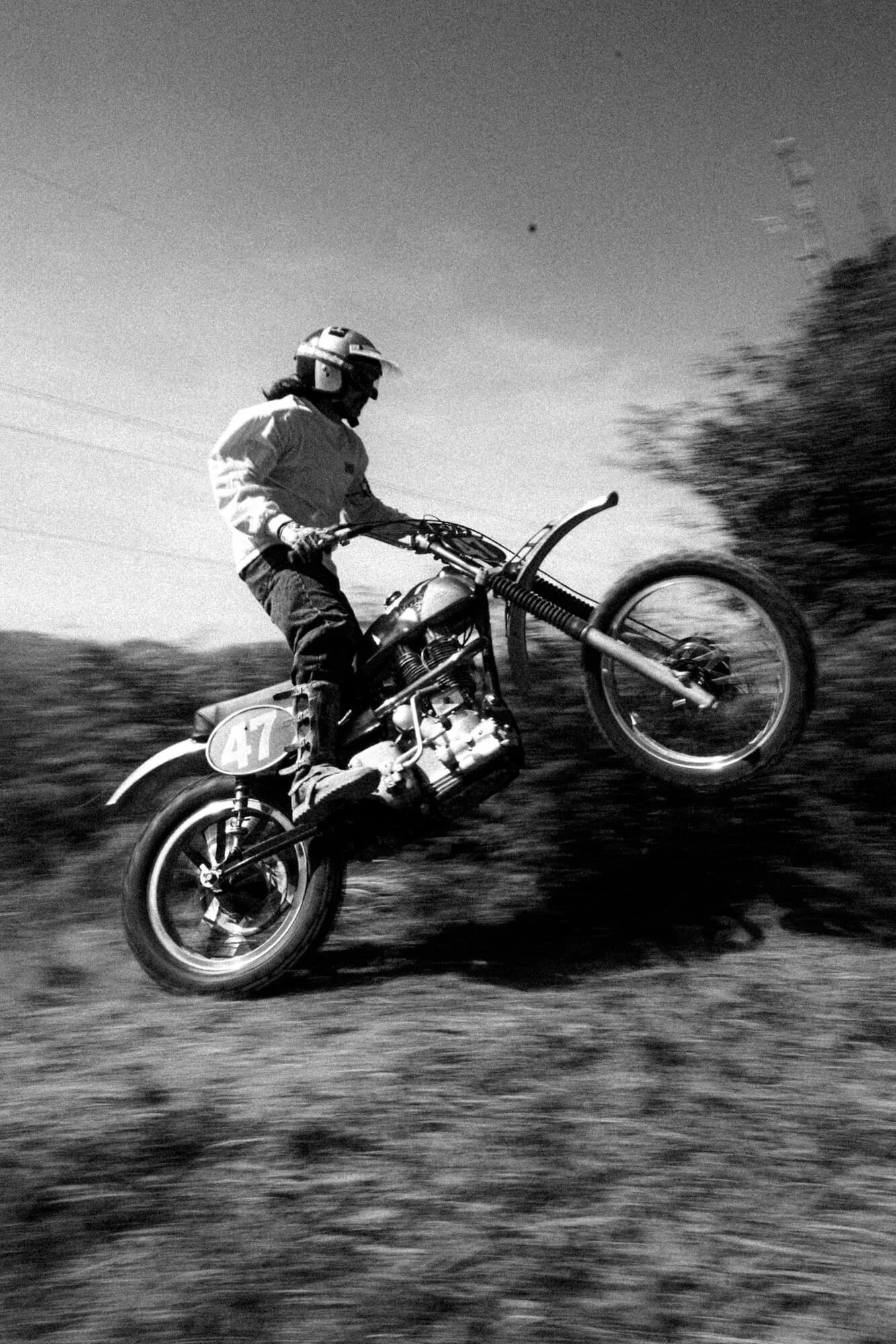 Black and white photo of a motocross rider in mid-air on a dirt bike, with the number 47 on the front