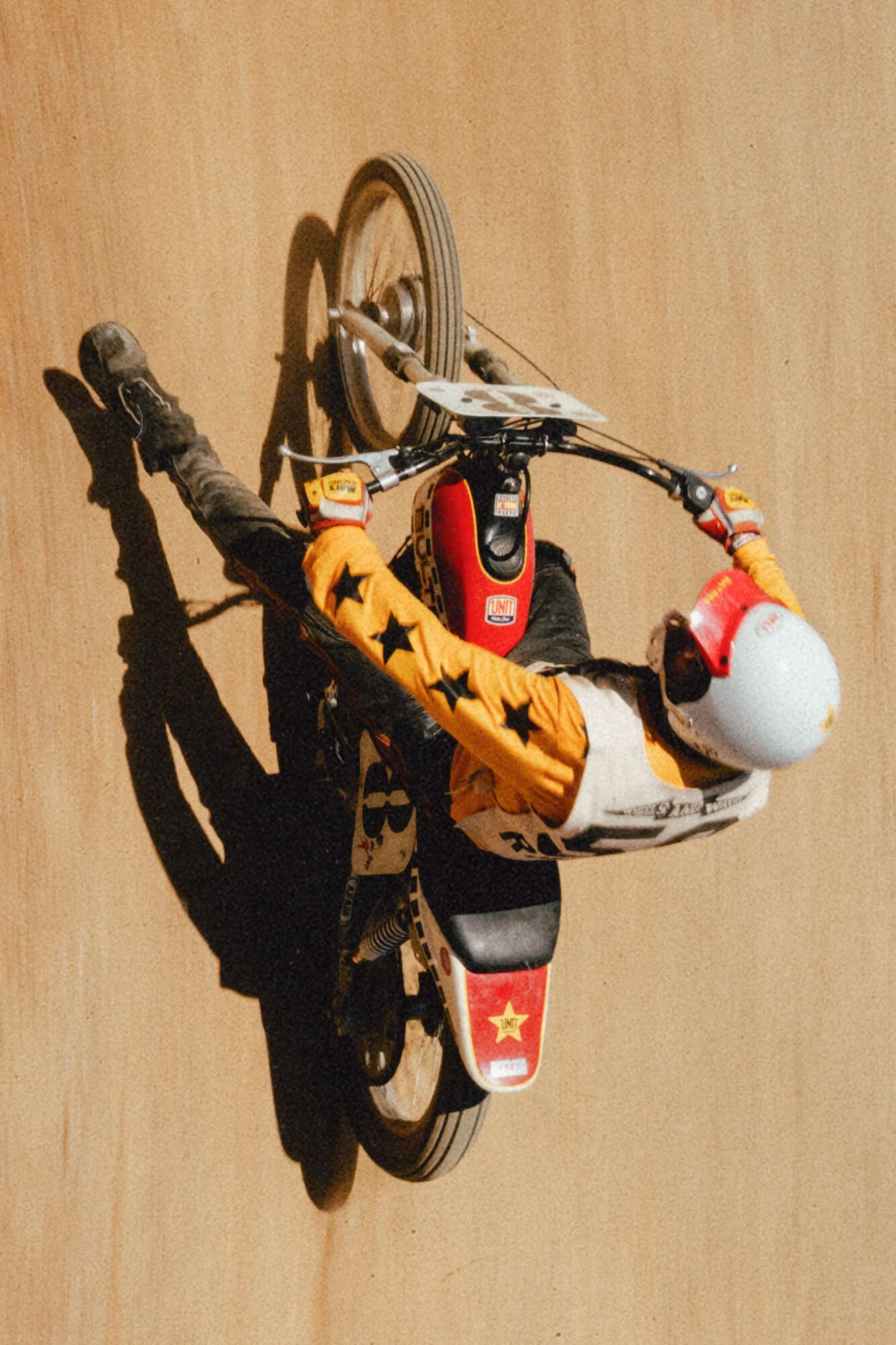 A child riding a red and white dirt bike indoors with a light brown wall in the background.