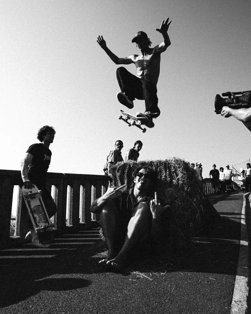 Un skateur en plein saut, entouré de spectateurs et d'une camera, lors d'un événement en plein air.
