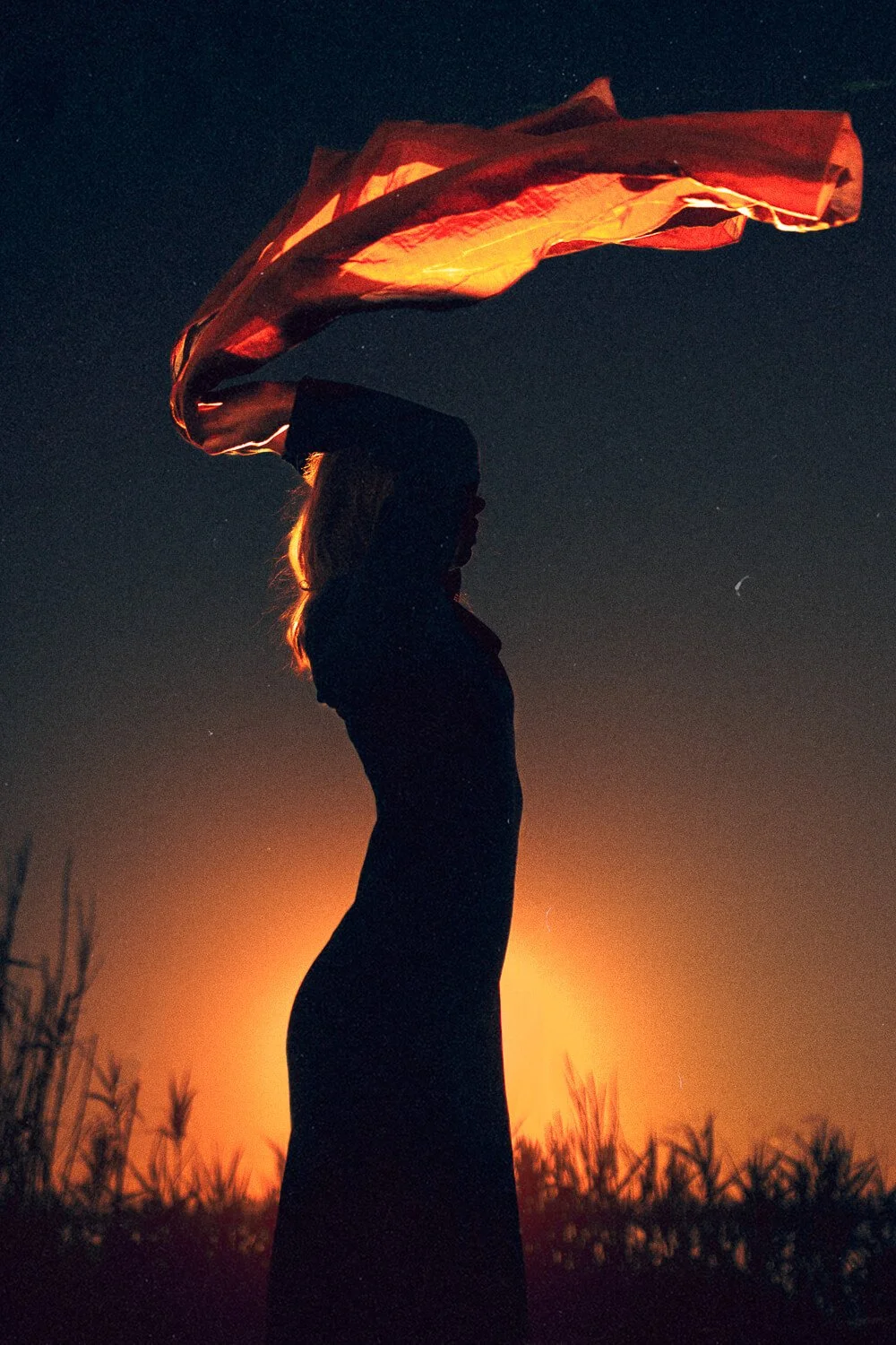 Silhouette of a woman holding a flag at sunset or sunrise with a starry sky in the background.