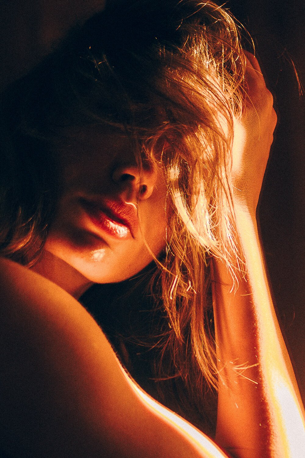 Close-up of a woman with tousled hair, lips slightly parted, illuminated by warm light.