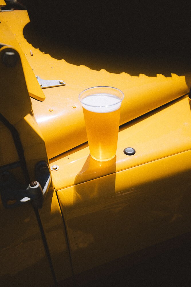 A pint of beer on a yellow industrial machine in sunlight.