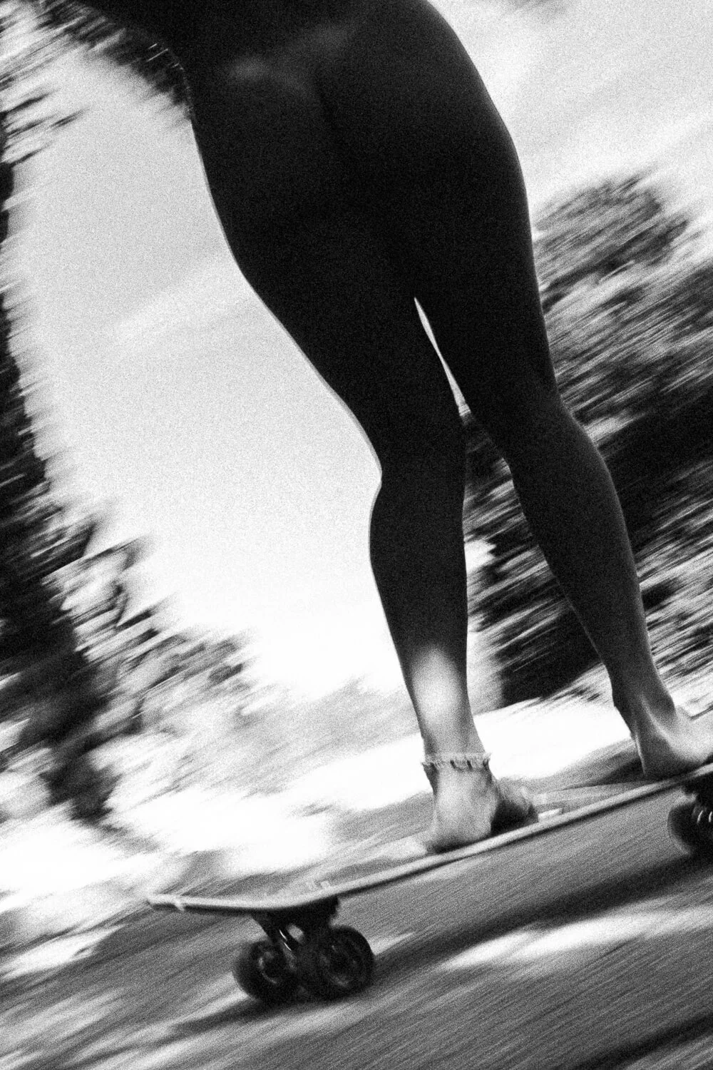A person riding a skateboard, captured from a low angle in motion, with blurred trees and sky in the background.