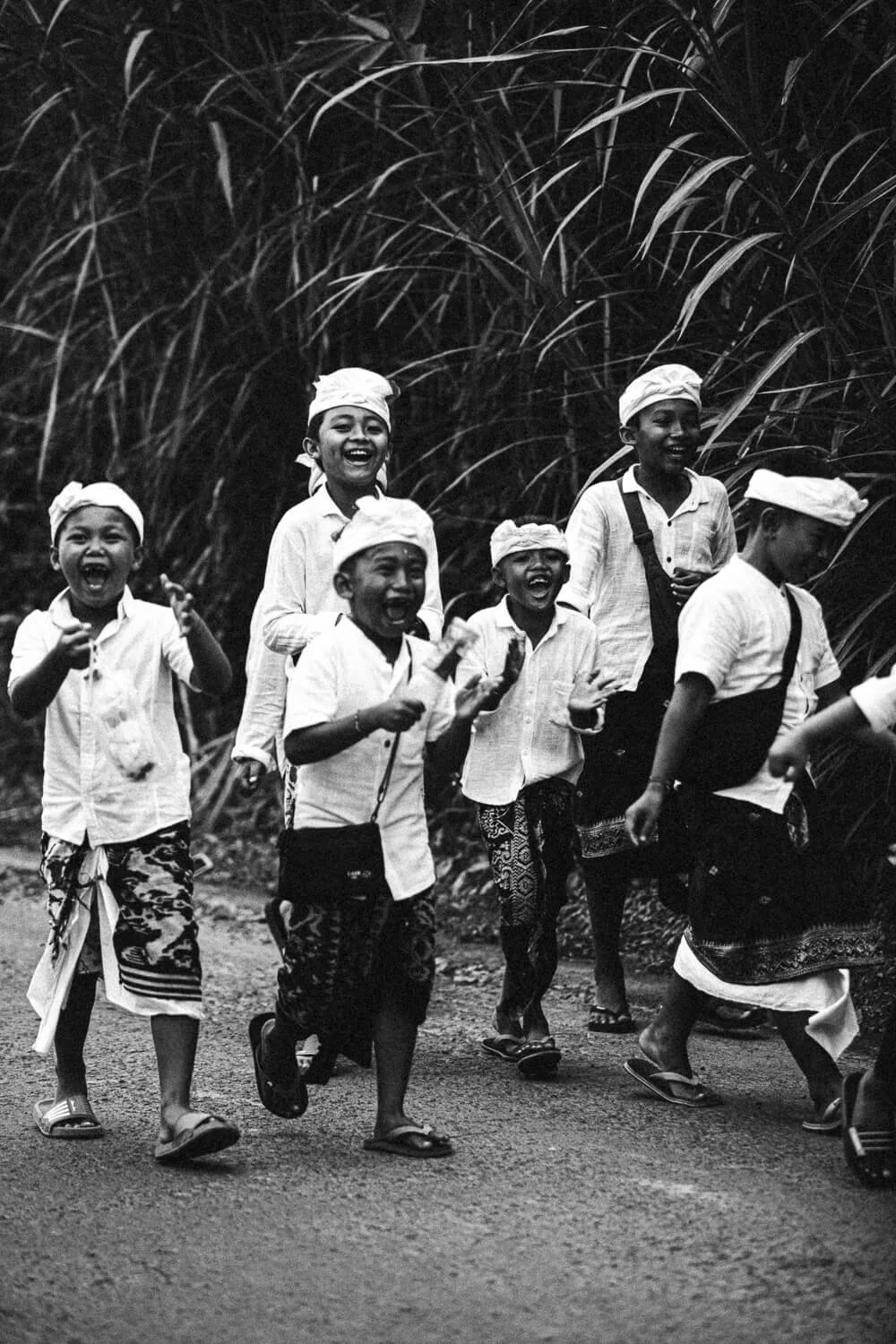 Groupe d'enfants souriants marchant ensemble sur un chemin, portant des vêtements traditionnels en zone rurale.