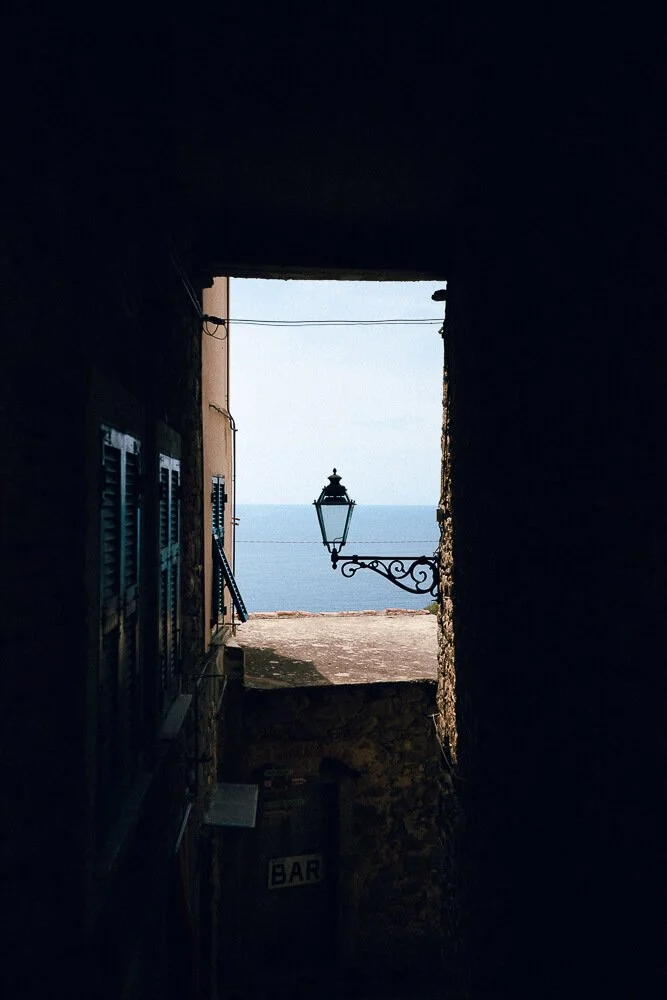 View of the sea framed by a dark stone archway with a streetlamp hanging outside and a sign that says 'BAR' at the bottom.