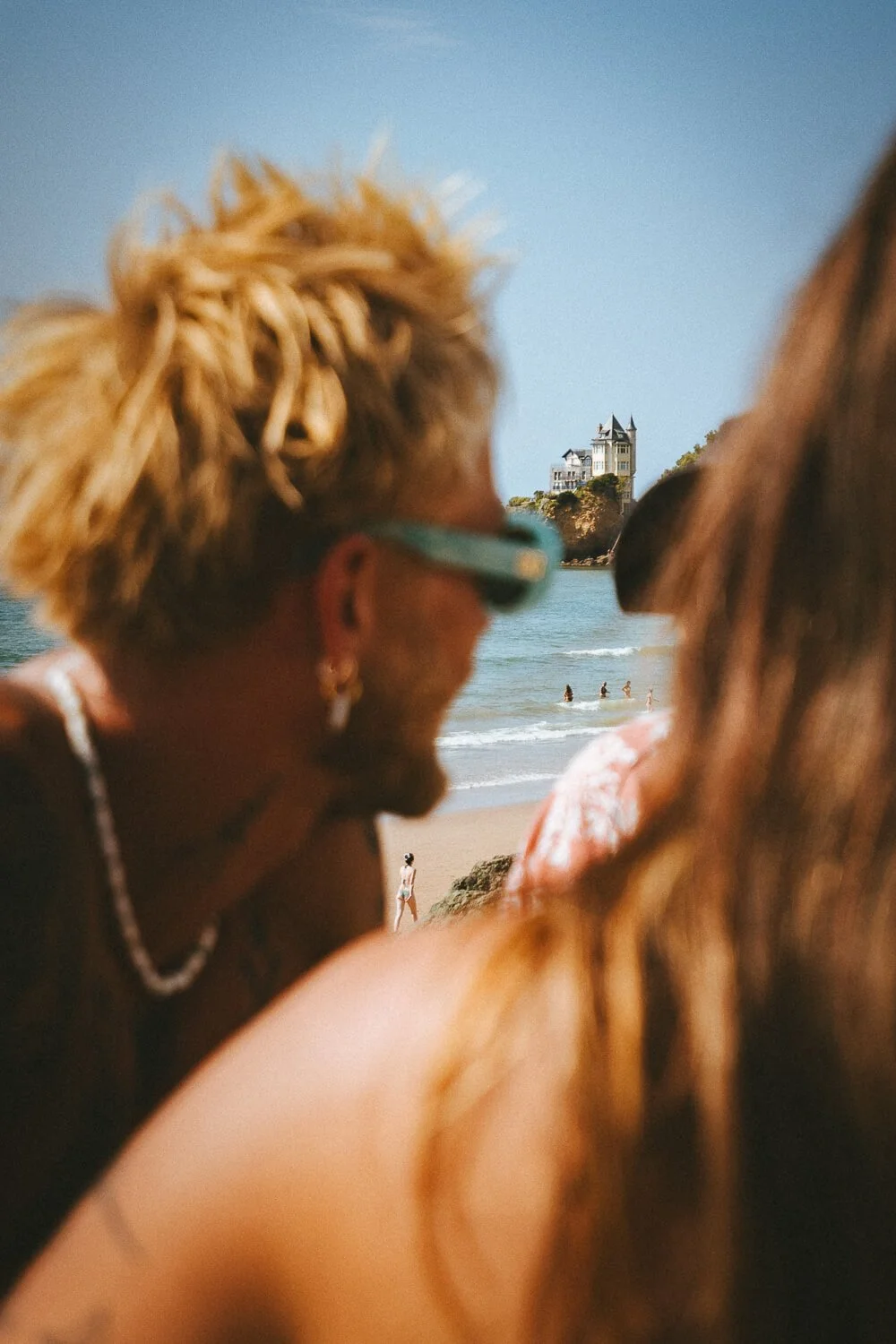 People at the beach, with houses on a hill in the background, and ocean waves.