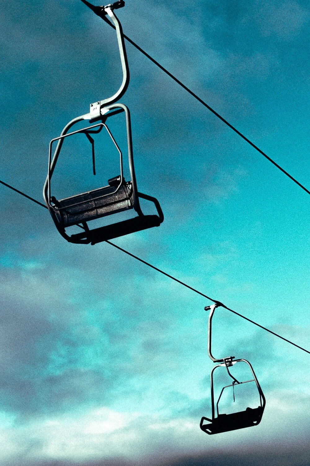 Empty ski lift chairs suspended in the sky against a cloudy blue background.