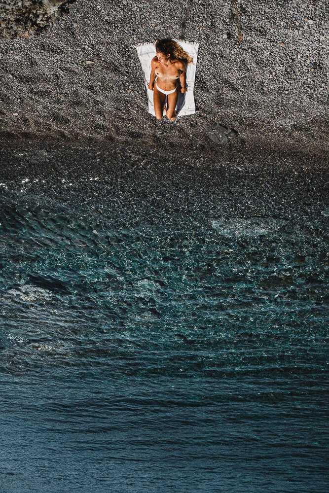 A woman lying on a towel on the beach, with the ocean and waves in the background.