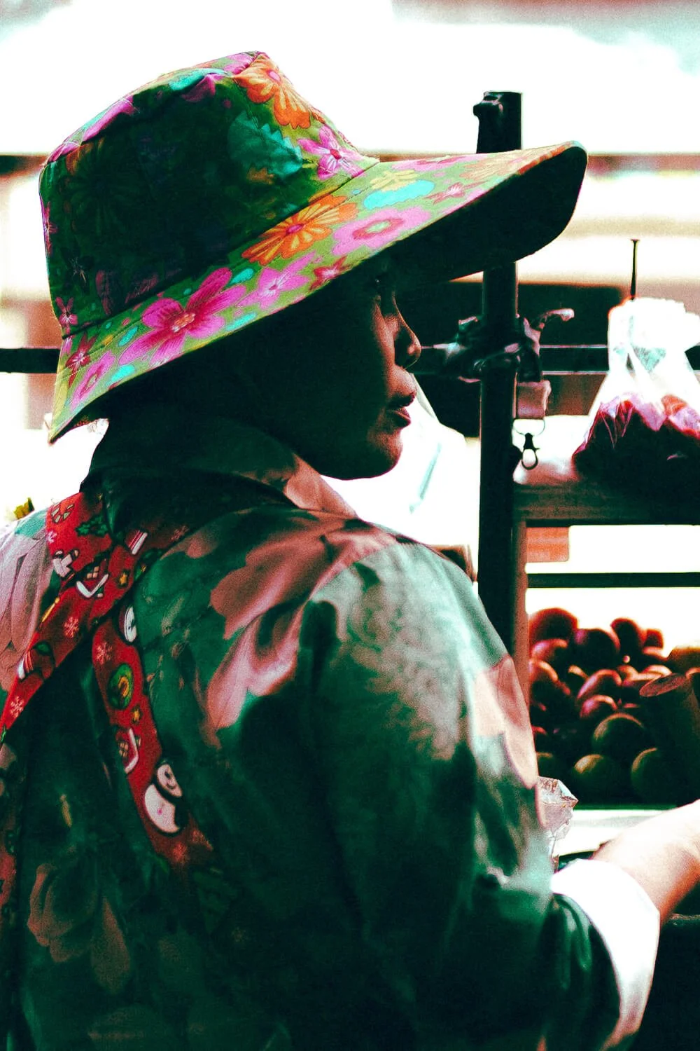 Une femme portant un chapeau à fleurs multicolores dans un marché, probablement vendant des fruits ou légumes.