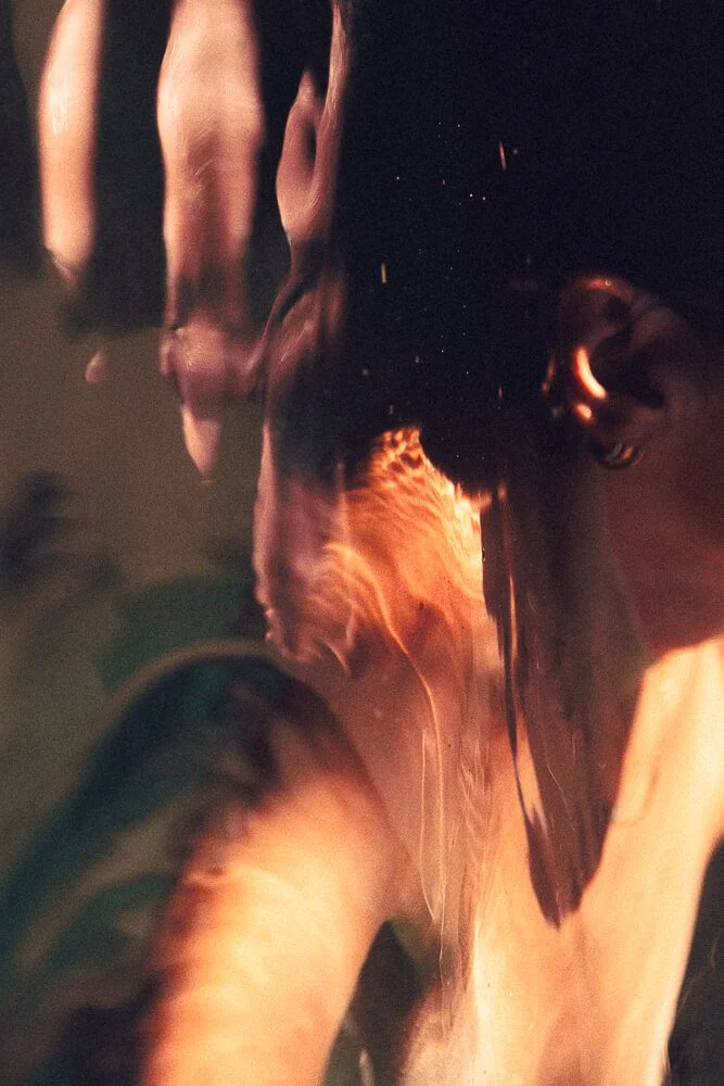 Close-up of a person's face partly submerged in water with ripples and reflections, creating an abstract effect.