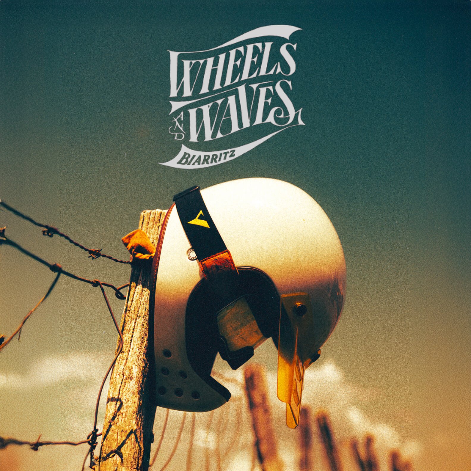 Un casque de vélo accroché à un poteau en bois, avec un ciel nuageux en arrière-plan, et un logo 'Wheels & Waves Biarritz' en haut.