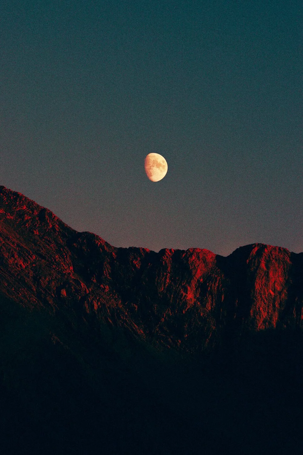 Lune visible dans le ciel au-dessus de montagnes rocheuses.