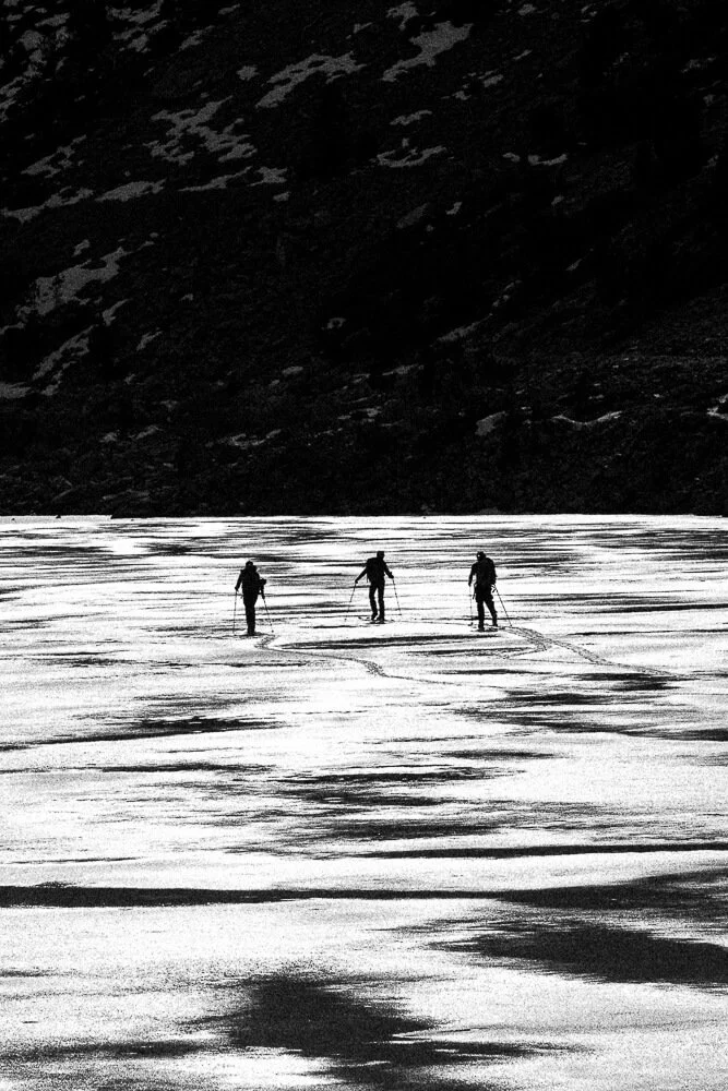 Three people cross a snowfield on skis with a mountain with snow in the background.