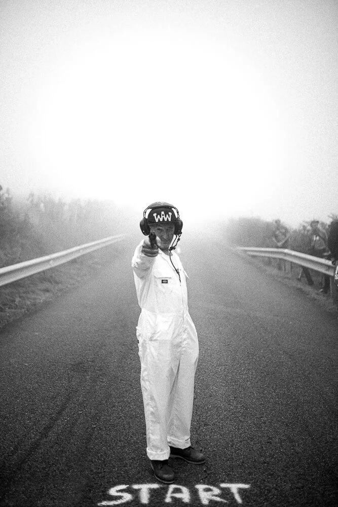 Person wearing white jumpsuit and helmet standing on a road with 'START' painted on the ground, pointing forward.