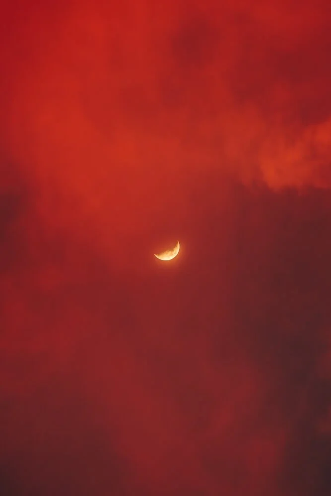 A crescent moon against a red, clouded sky.