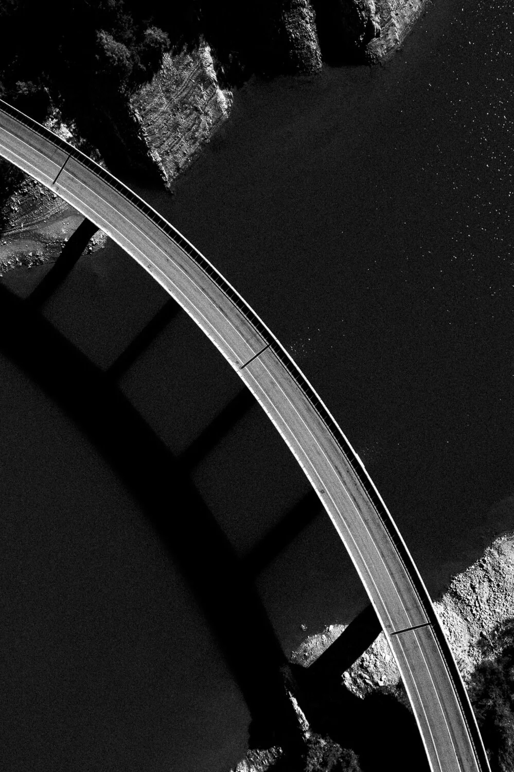 Une image en noir et blanc montrant un pont au-dessus d'une rivière, avec un reflet net de ses ombres sur l'eau.