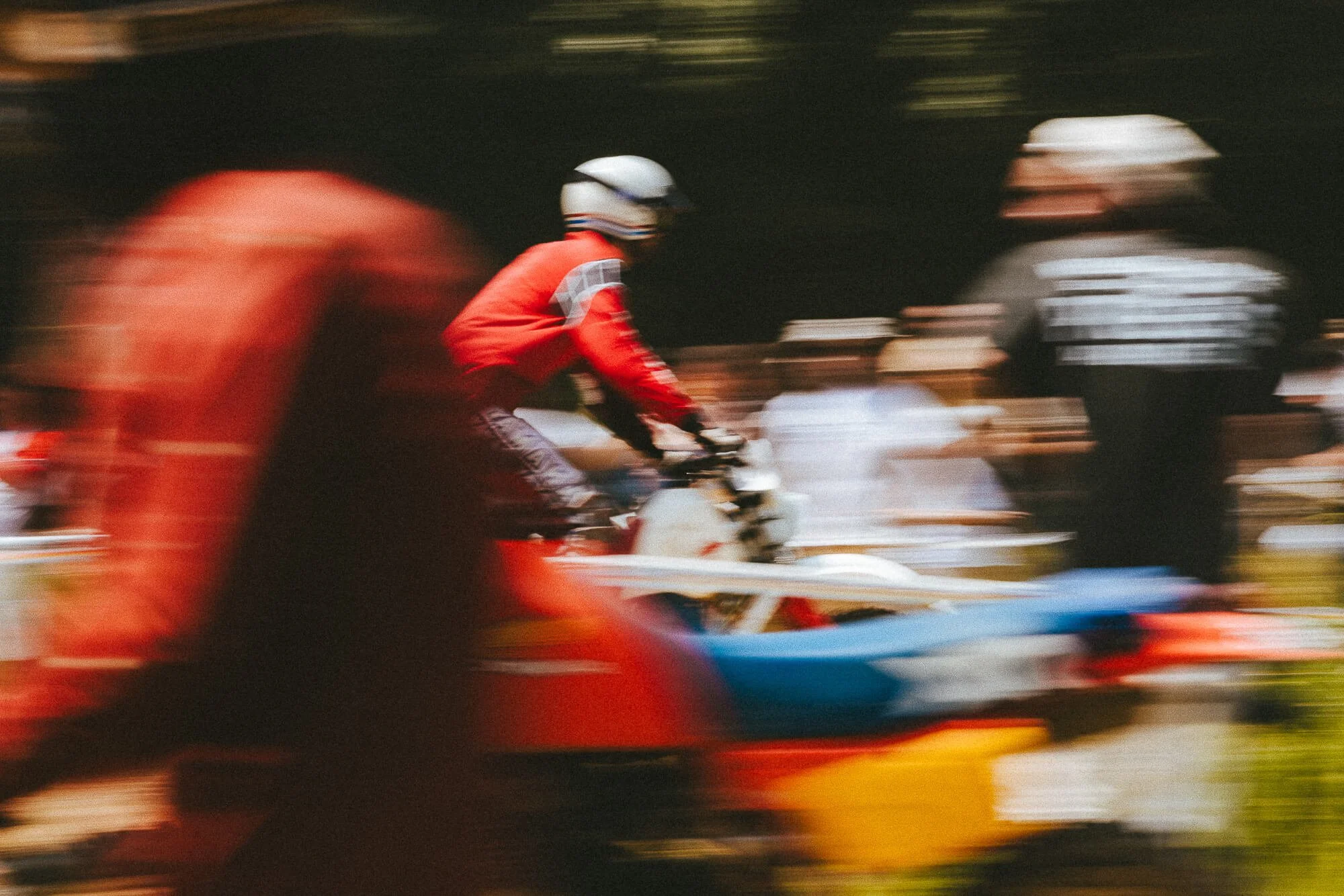 Une personne en casque et vêtue de rouge, roulant en moto ou scooter rapidement, avec un arrière-plan flou.