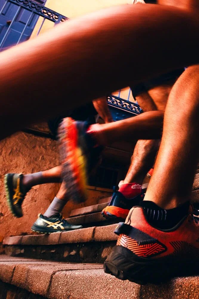 Close-up of people running up outdoor stone stairs, wearing athletic shoes, with a fence in the background.