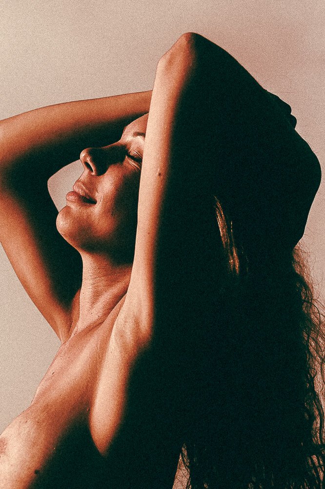 A woman with her eyes closed, lips slightly parted, arms raised above her head, and hair flowing, appearing to be enjoying a moment of relaxation or serenity.