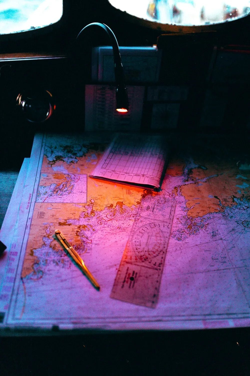 Une carte maritime avec un compas, une règle, un carnet ouvert, un stylo, et une incandescence, sur une surface de bureau.