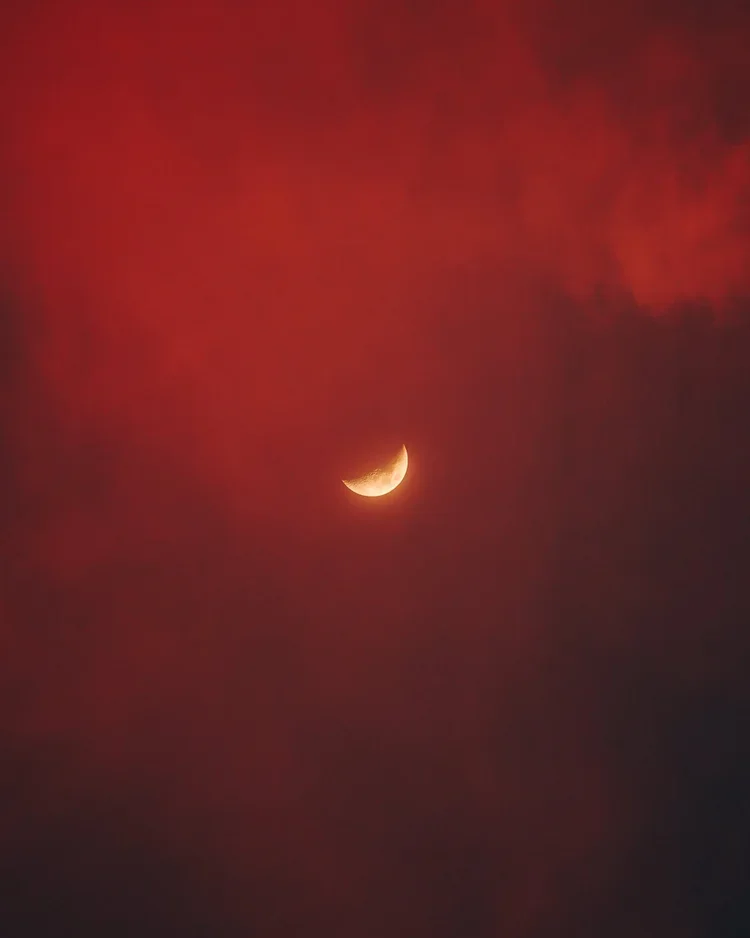 Lune en croissant dans un ciel rouge avec des nuages