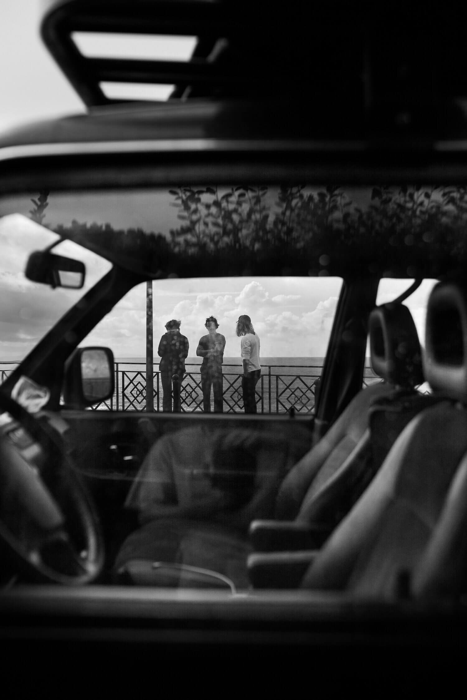 Trois personnes debout près d'une balustrade, vues depuis l'intérieur d'une voiture.