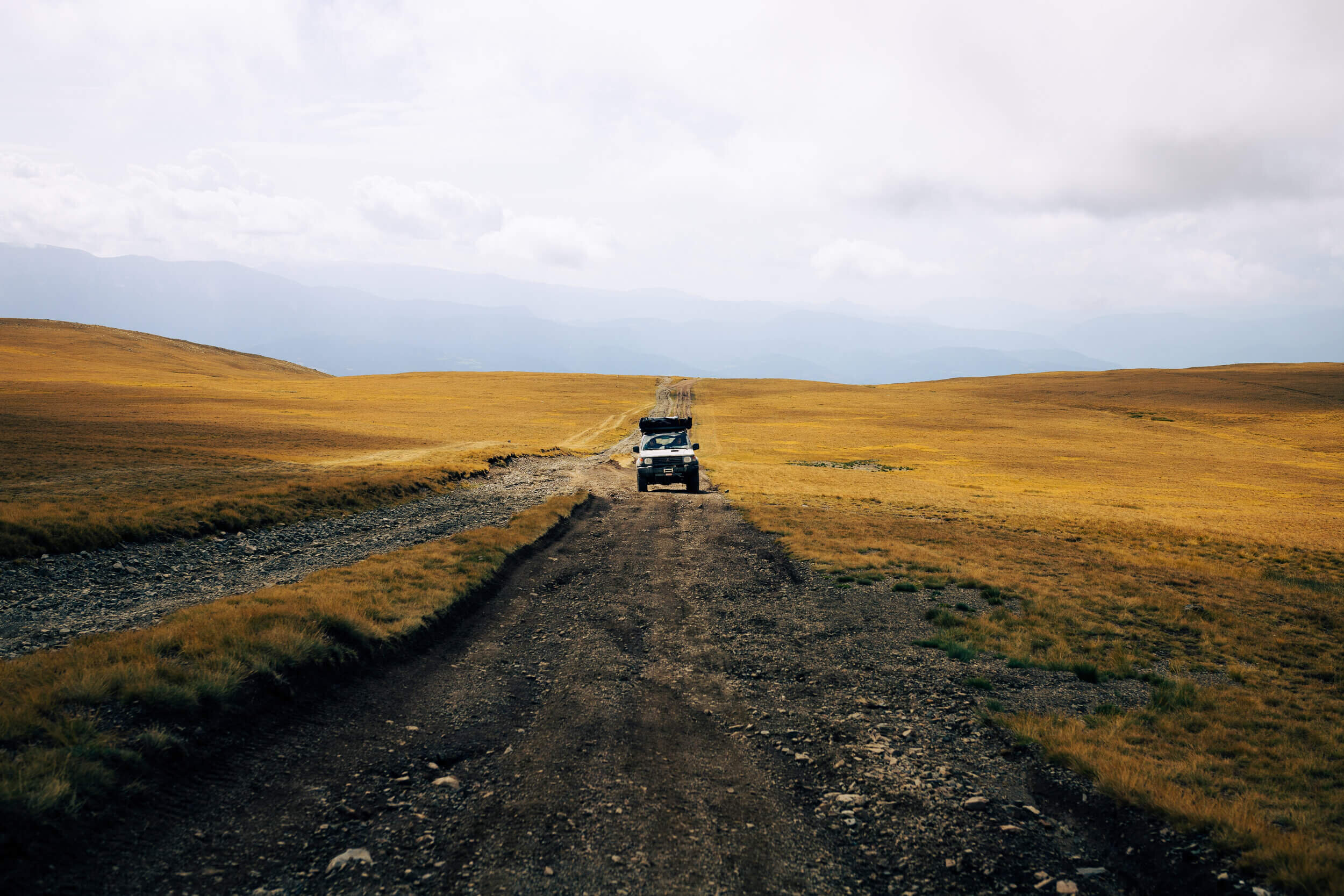 4x4 sur une route de terre dans un paysage de prairie avec ciel nuageux.