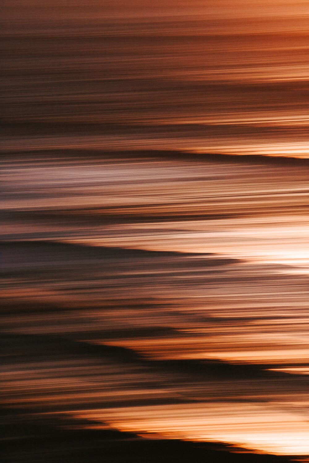 Blurred lines of sunset or sunrise over water with warm orange and pink hues