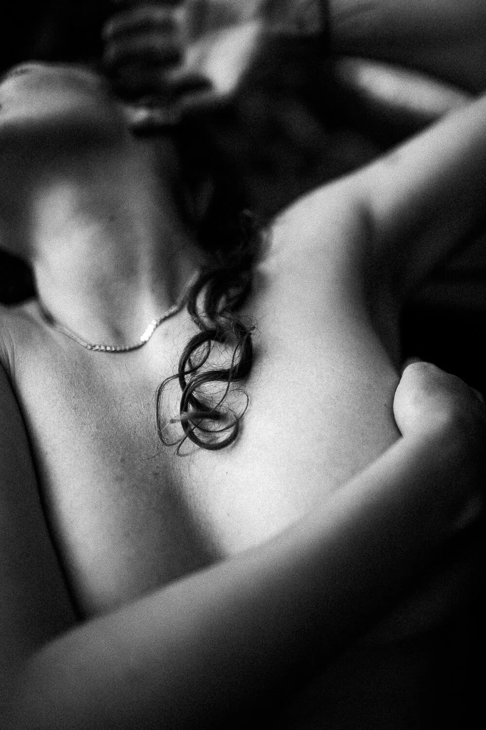 Black and white close-up of a woman's shoulder, neck, and part of her face, with her hand resting on her shoulder and a necklace around her neck.