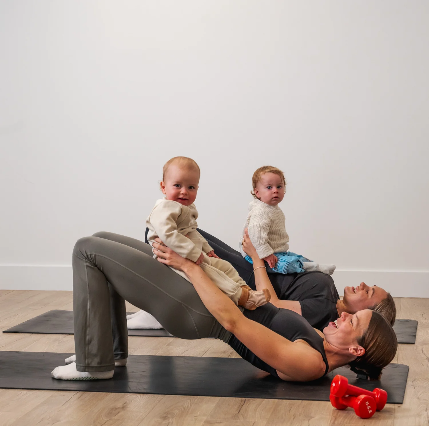 Two mums doing glute bridges with their babies resting on them