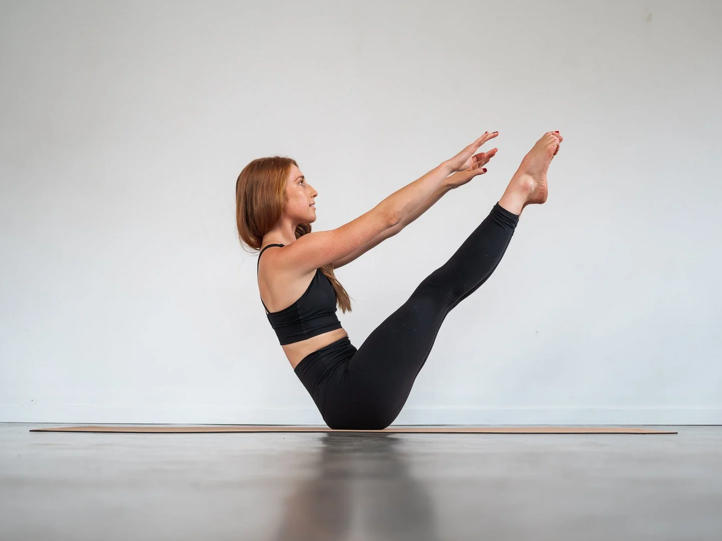Woman in black workout clothes performing a yoga pose on a mat in a minimalist studio.