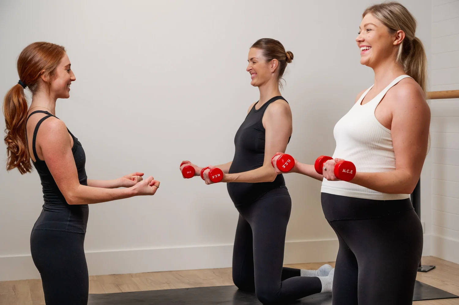 Pregnant women training with dumbbells while Bridget coaches