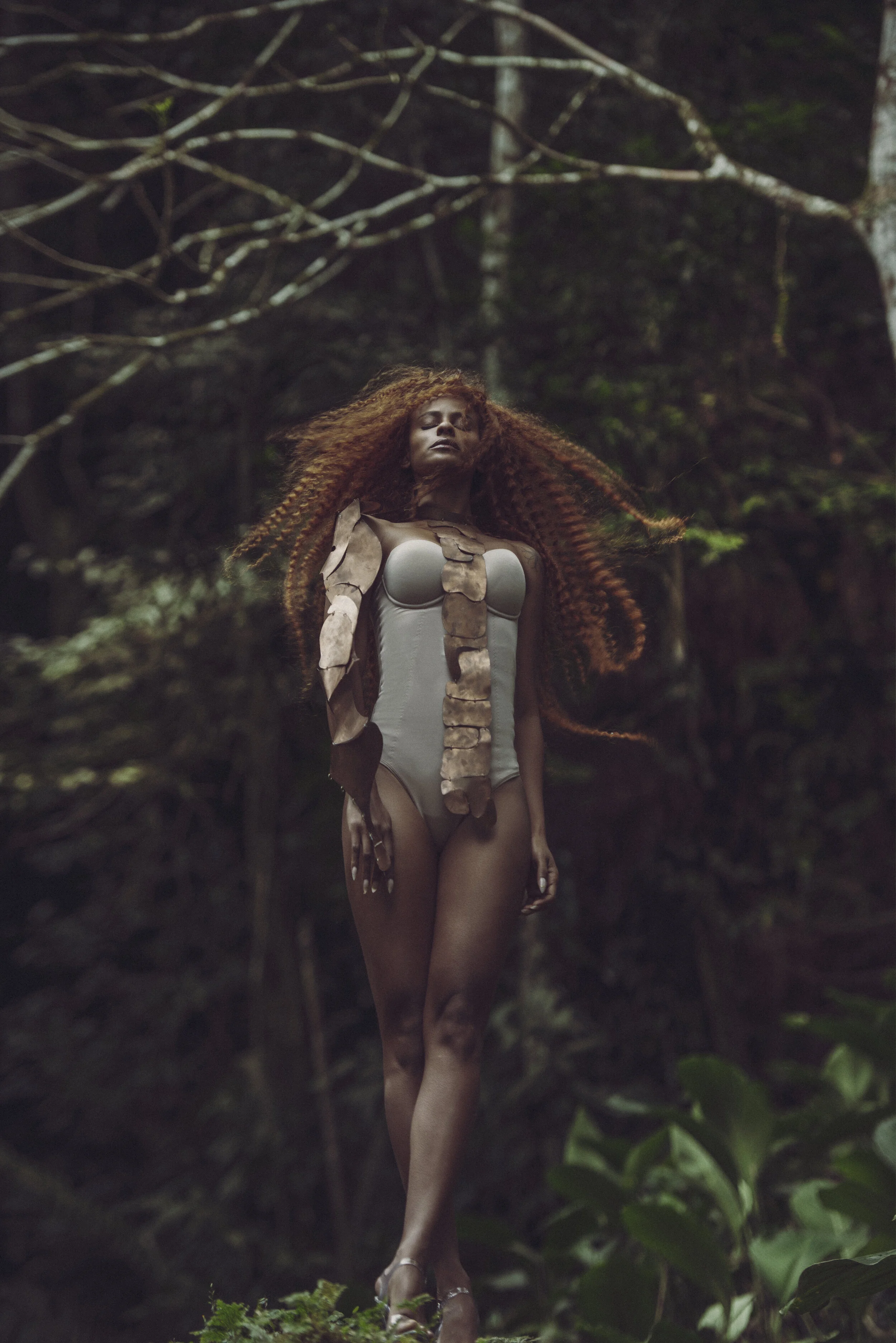 Mulher com cabelo encaracolado e vestimenta de caveira, caminando na floresta.