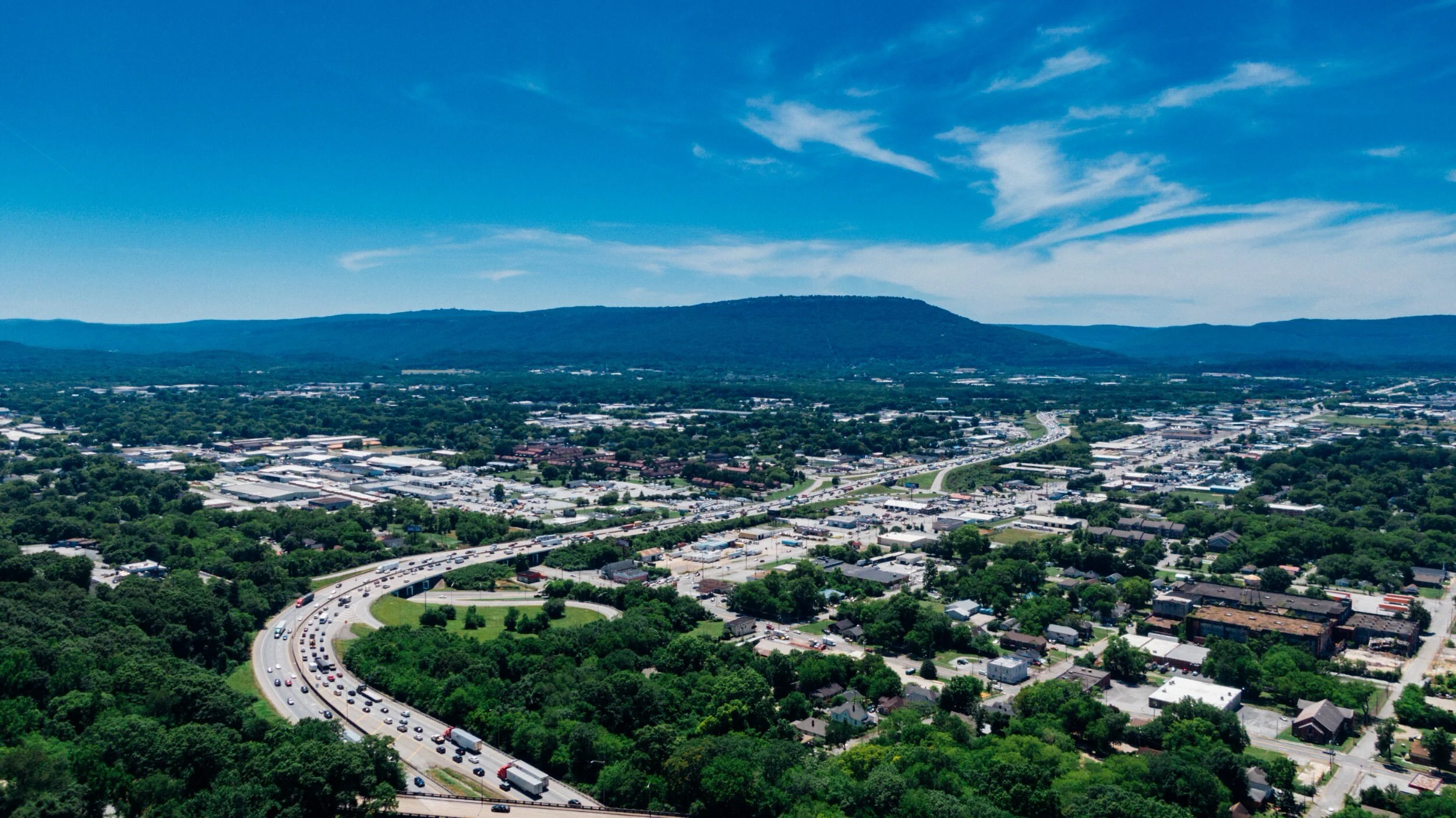 Aerial view of Tennessee city with highway traffic, green trees and distant blue mountains