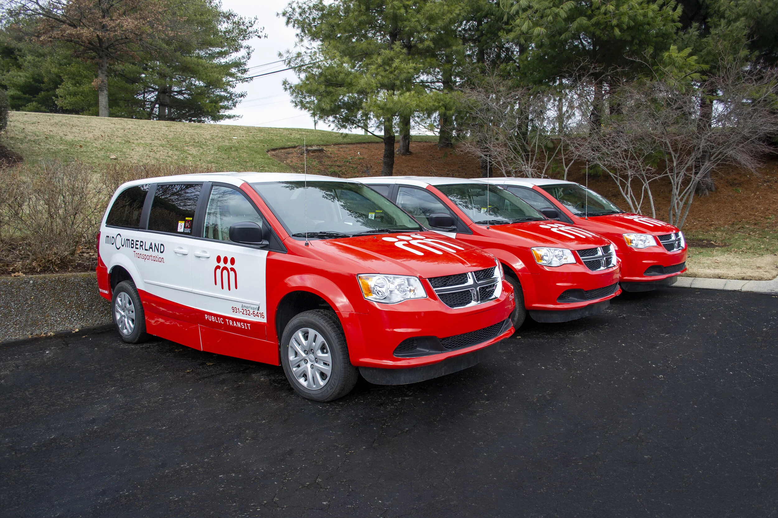 Row of red and white Mid-Cumberland public transit minivans parked outdoors
