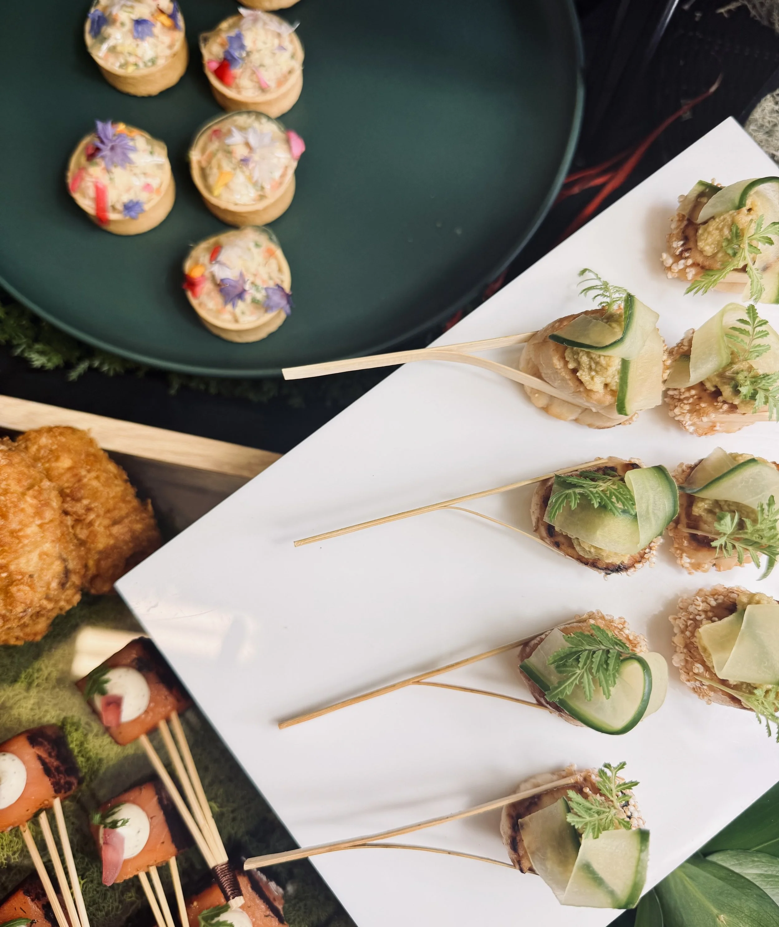 Assortiment de petits plats et canapés élégants avec des garnitures végétales, des fleurs comestibles, et des présentations artistiques, sur des plateaux de service.